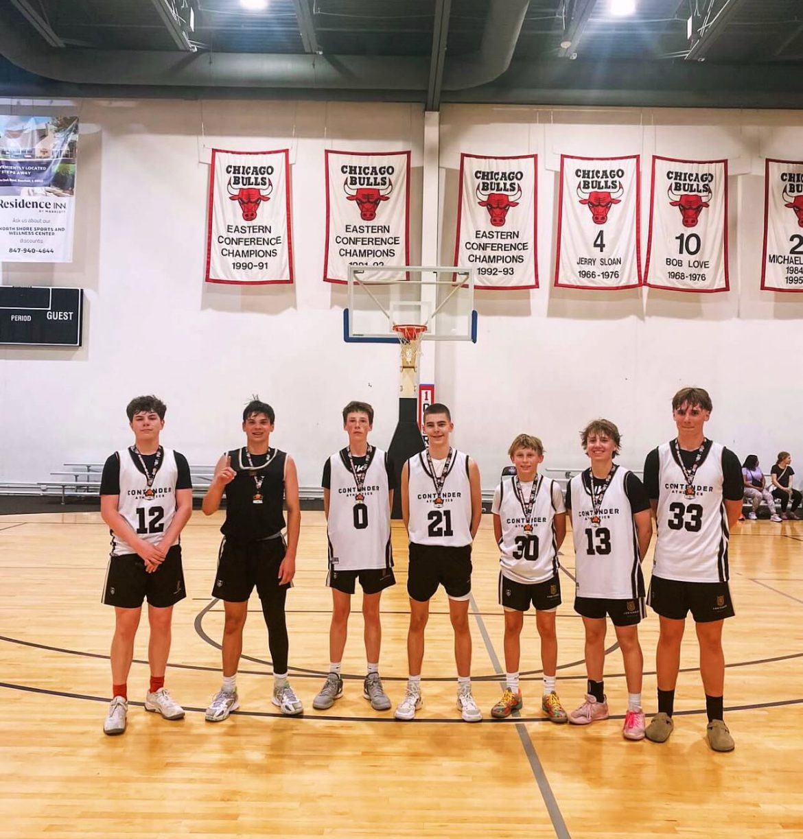 Youth basketball team posing on court under championship banners.