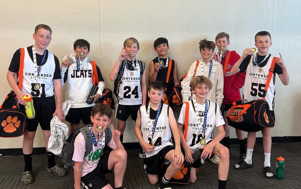 Group of young men posing with medals and jerseys indoors.