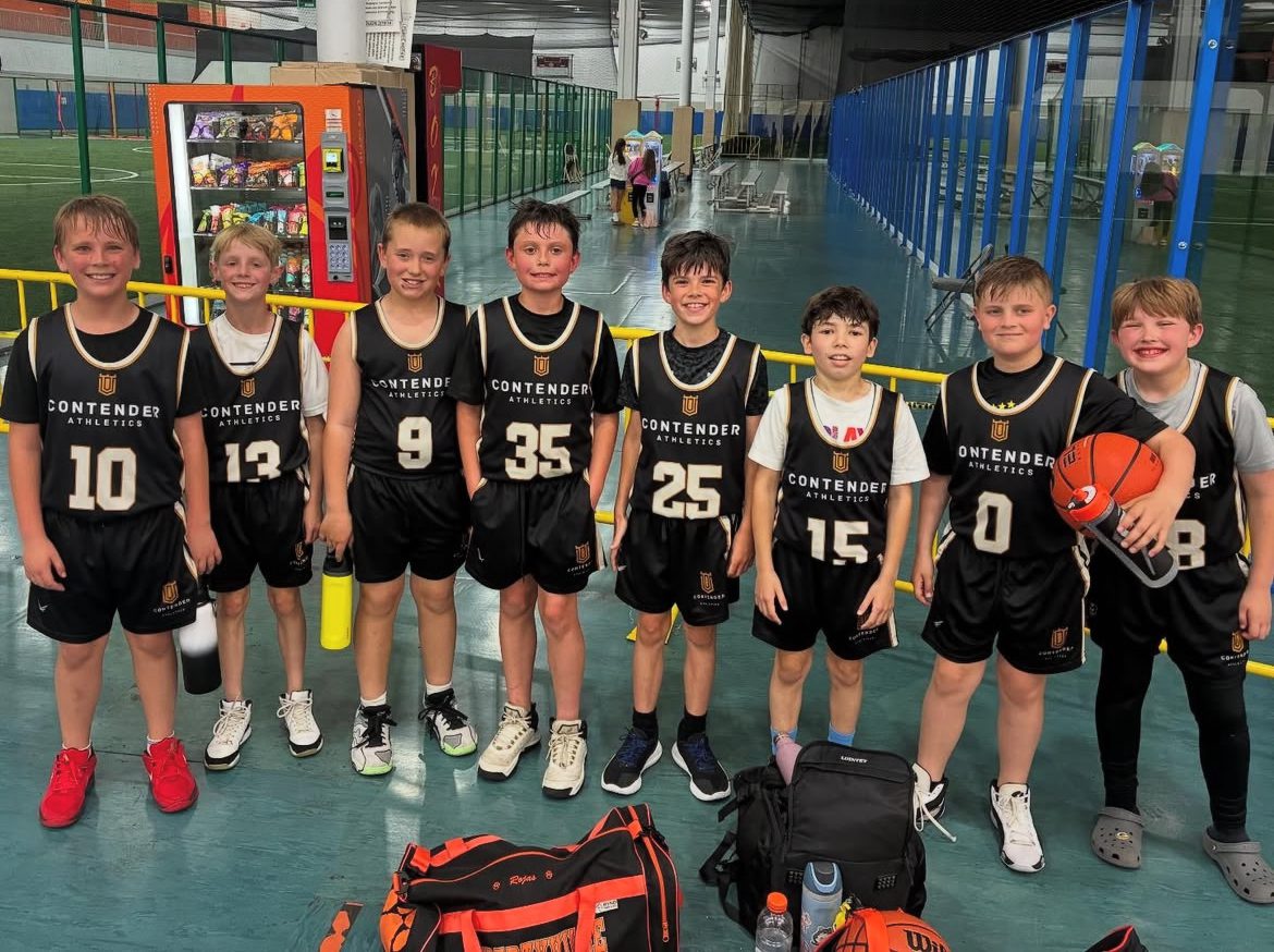 Youth basketball team posing in black uniforms indoors.
