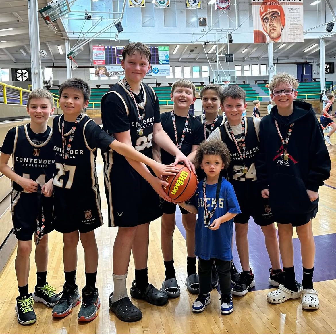 Youth basketball team posing with a young fan in a gymnasium.
