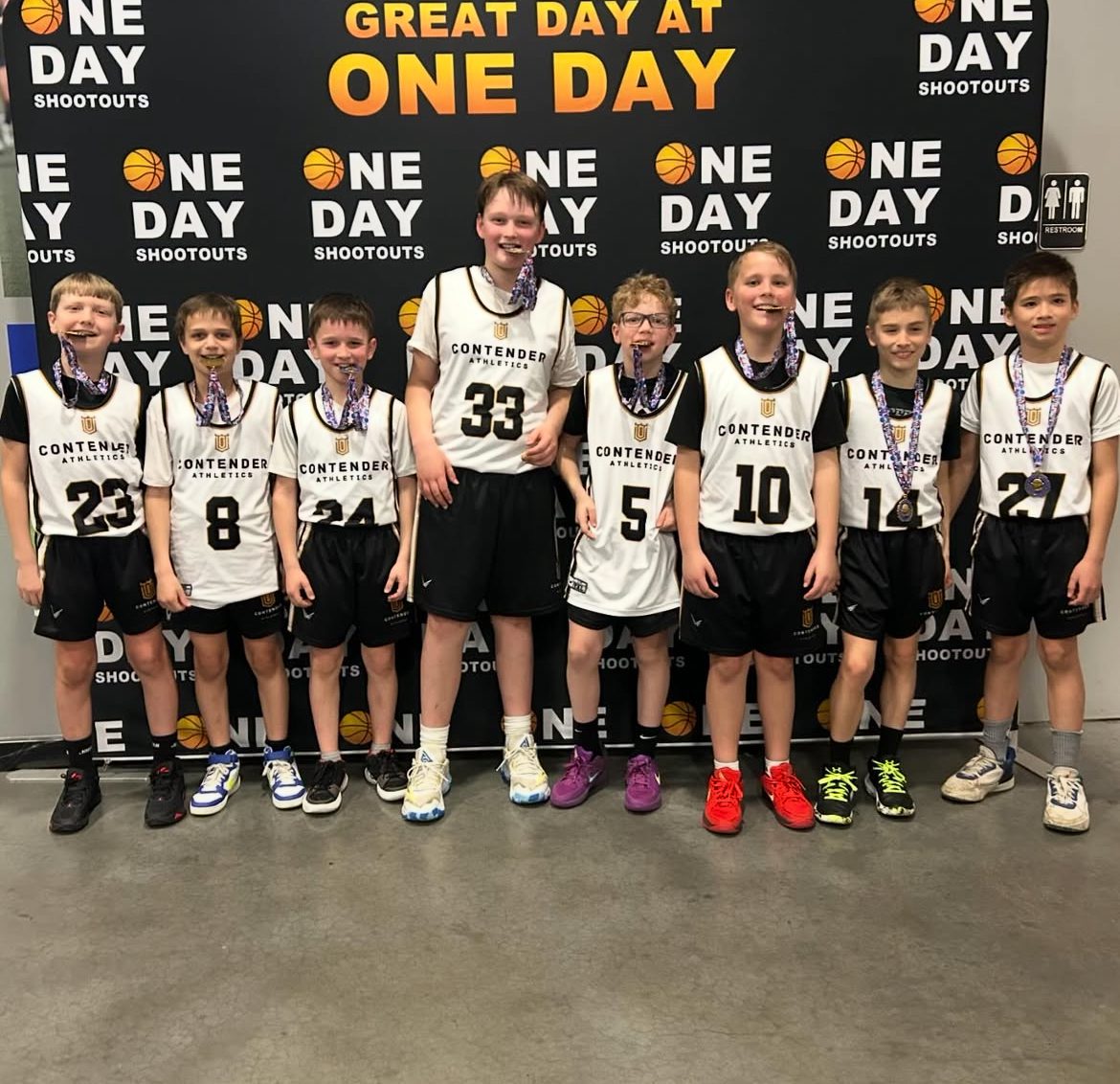 Youth basketball team posing indoors with medals and trophies.