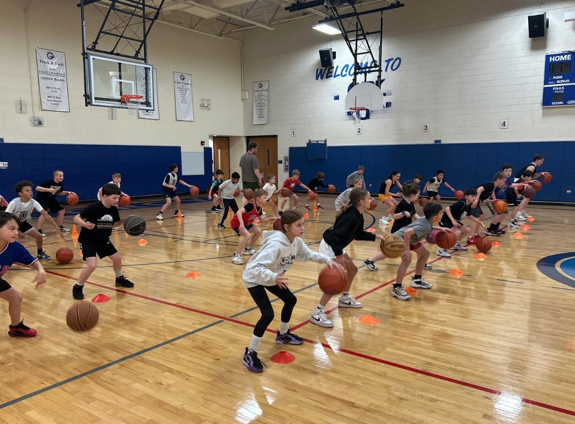 Children practicing basketball drills in a gymnasium.